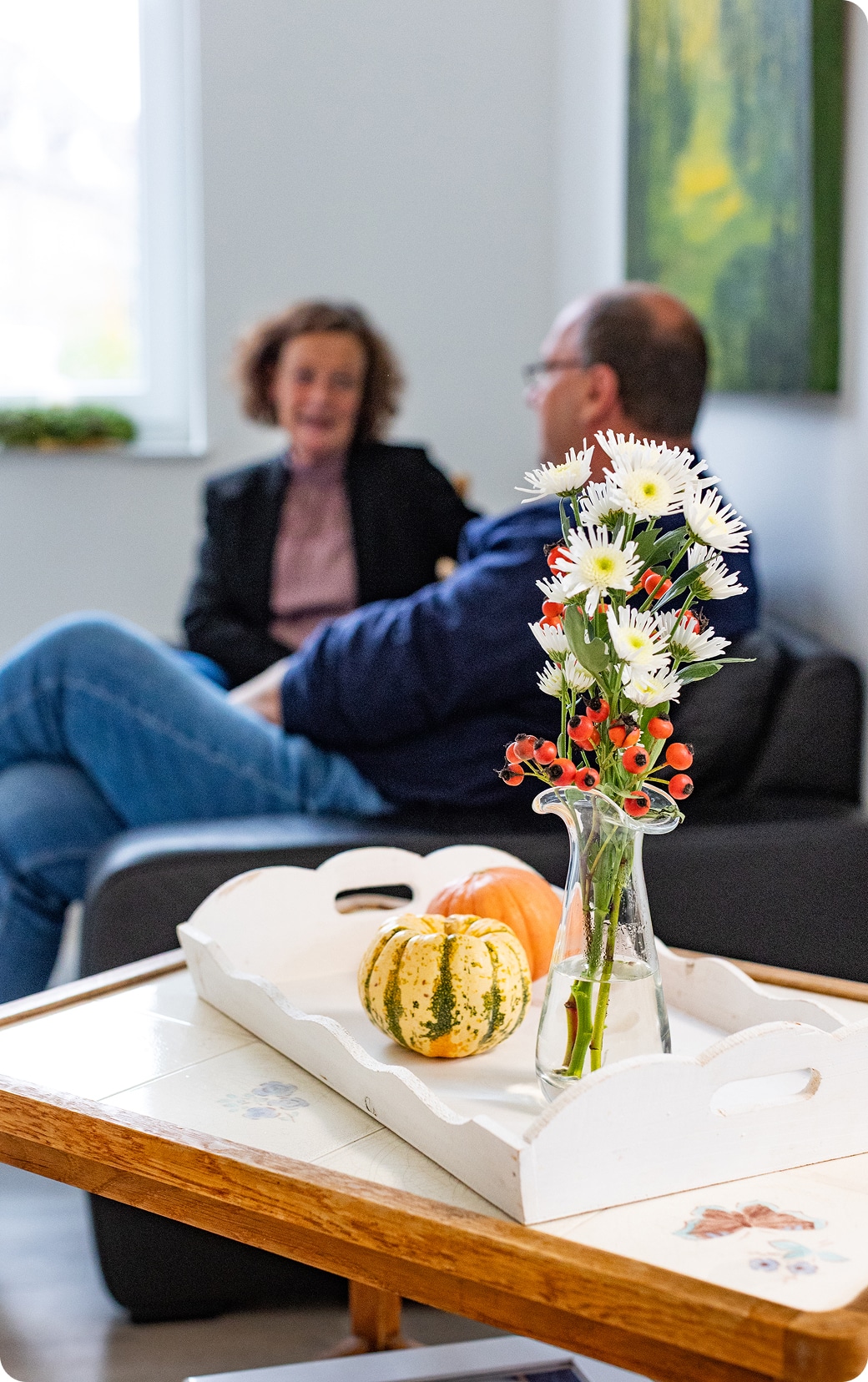 Pflegegespräch zu Hause mit ruhiger Herbstdekoration und Blumenvase im Vordergrund
