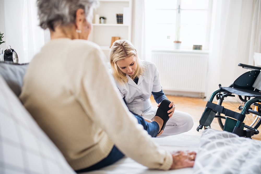 Pflegekraft hilft einer älteren Patientin einfühlsam beim Anziehen zu Hause